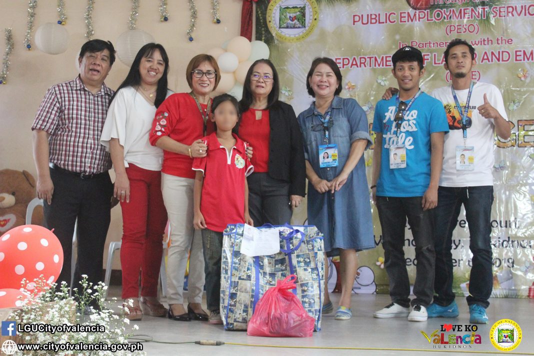 The benefactors, together with the PESO Manager Elna B. Guzman (3rd from left) and City Mayor Azucena P. Huervas (center), hand-over the gifts to child laborer as written on her wish list for the Project Angel Tree on 6 December 2019 at the LGU Valencia Covered Court, Valencia City, Bukidnon. (PESO Office, LGU-Valencia City)